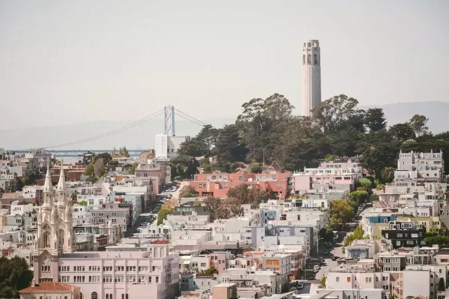 贝博体彩app的Coit Tower，背景是海湾大桥，全景是一座被房屋覆盖的山丘.